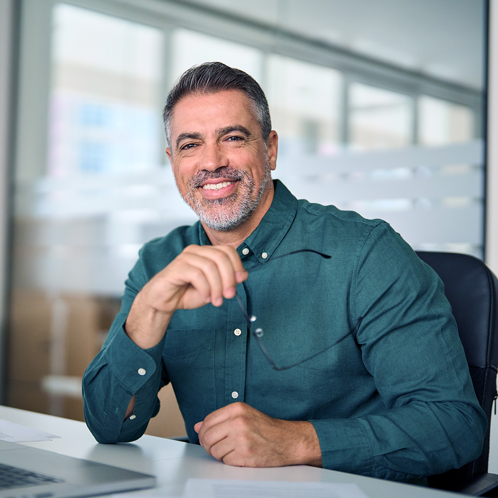 A man in a green shirt sitting at a desk with a laptop